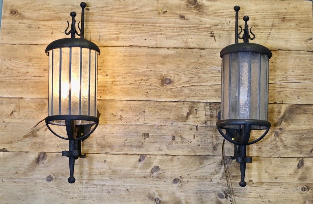 A pair of large black wrought iron wall lanterns featuring cylindrical glass shades with vertical metal bars and decorative finials at the top and bottom. View II