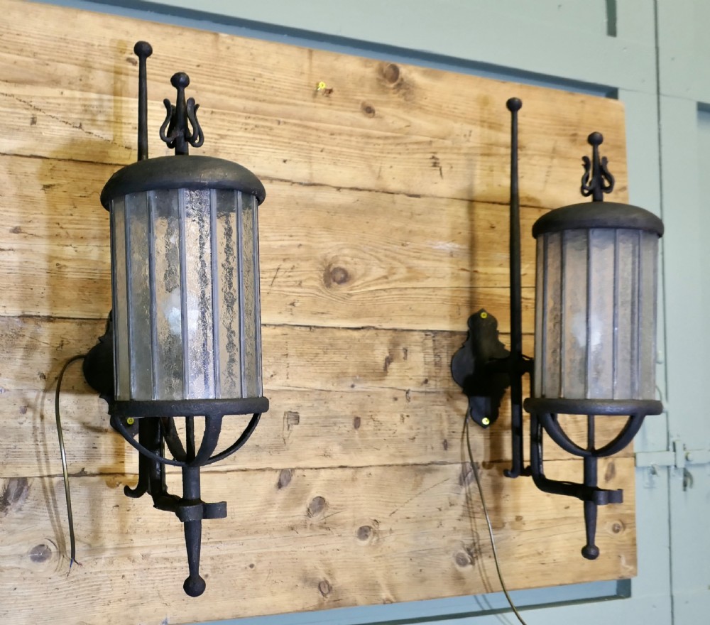 A pair of large black wrought iron wall lanterns featuring cylindrical glass shades with vertical metal bars and decorative finials at the top and bottom. View III