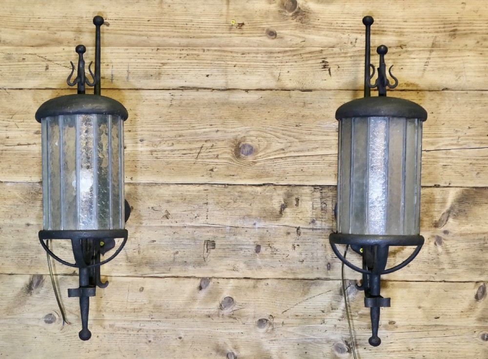 A pair of large black wrought iron wall lanterns featuring cylindrical glass shades with vertical metal bars and decorative finials at the top and bottom. View IV