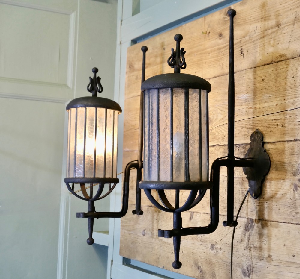 A pair of large black wrought iron wall lanterns featuring cylindrical glass shades with vertical metal bars and decorative finials at the top and bottom. View VII