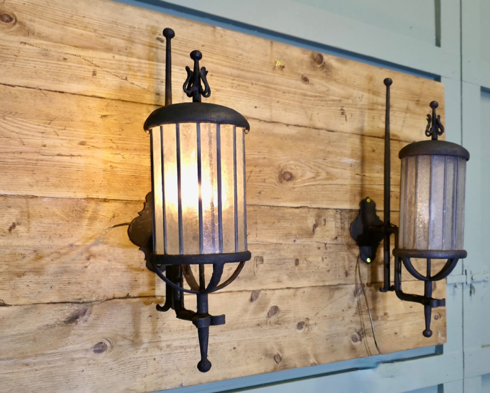 A pair of large black wrought iron wall lanterns featuring cylindrical glass shades with vertical metal bars and decorative finials at the top and bottom. View VIII