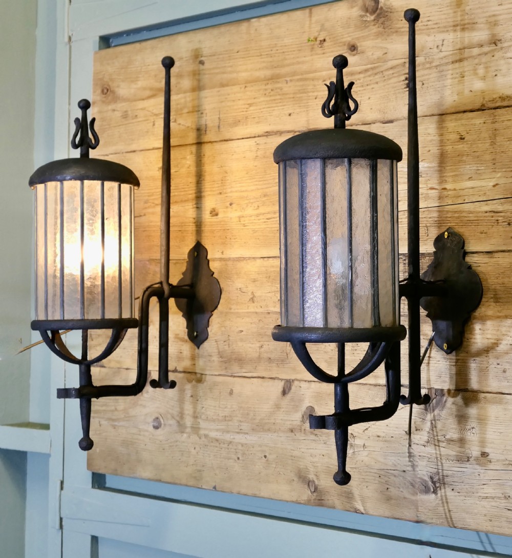 A pair of large black wrought iron wall lanterns featuring cylindrical glass shades with vertical metal bars and decorative finials at the top and bottom. View IX