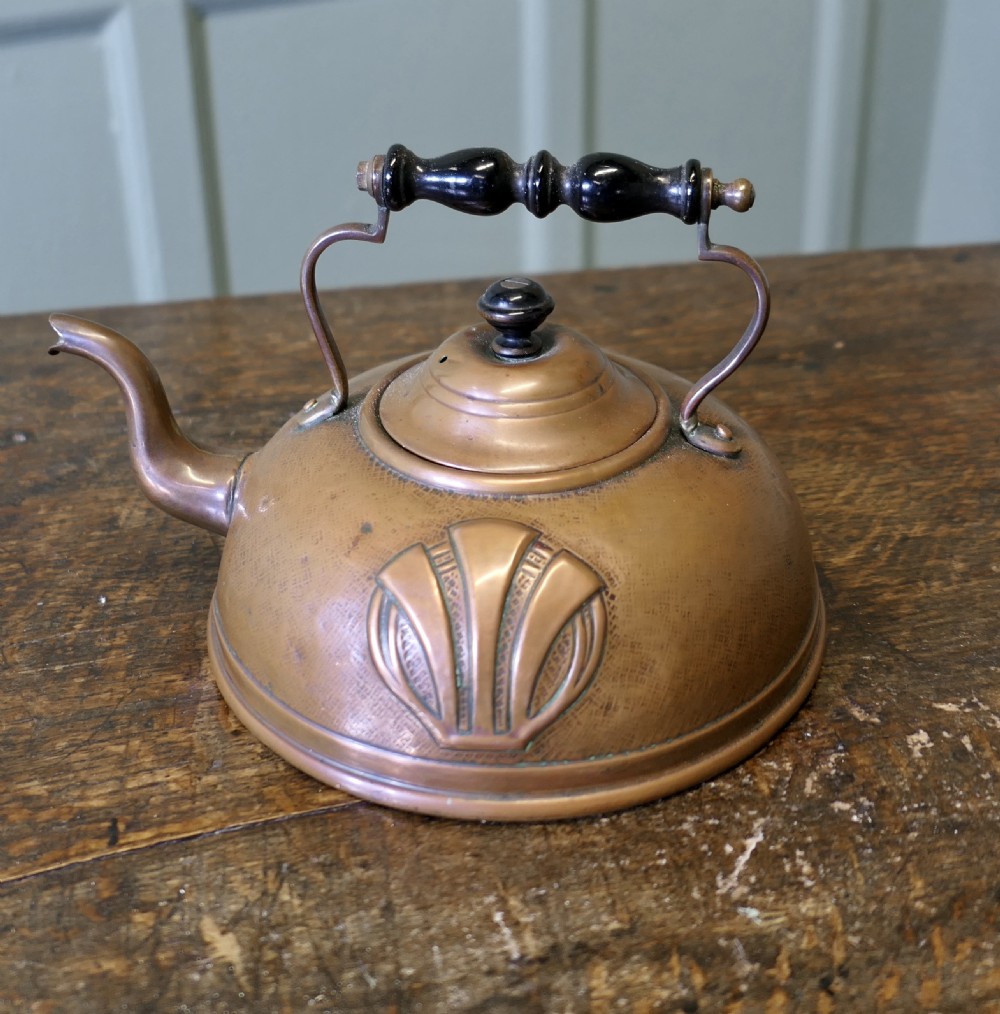 An Arts and Crafts copper kettle with a stylised relief shell motif, gooseneck spout, and turned black wooden handle. View II