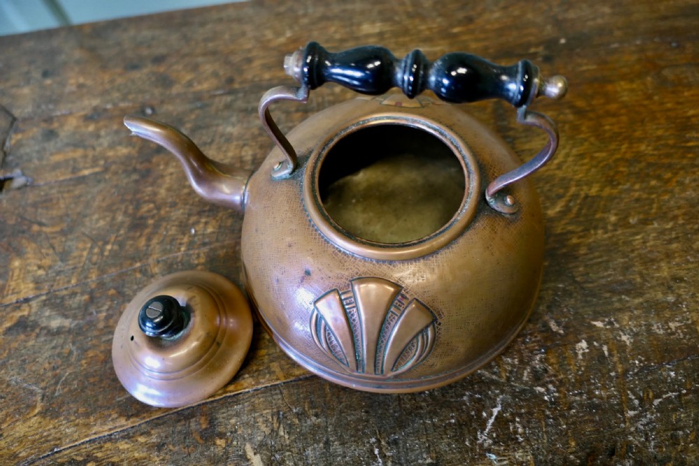 An Arts and Crafts copper kettle with a stylised relief shell motif, gooseneck spout, and turned black wooden handle. View III