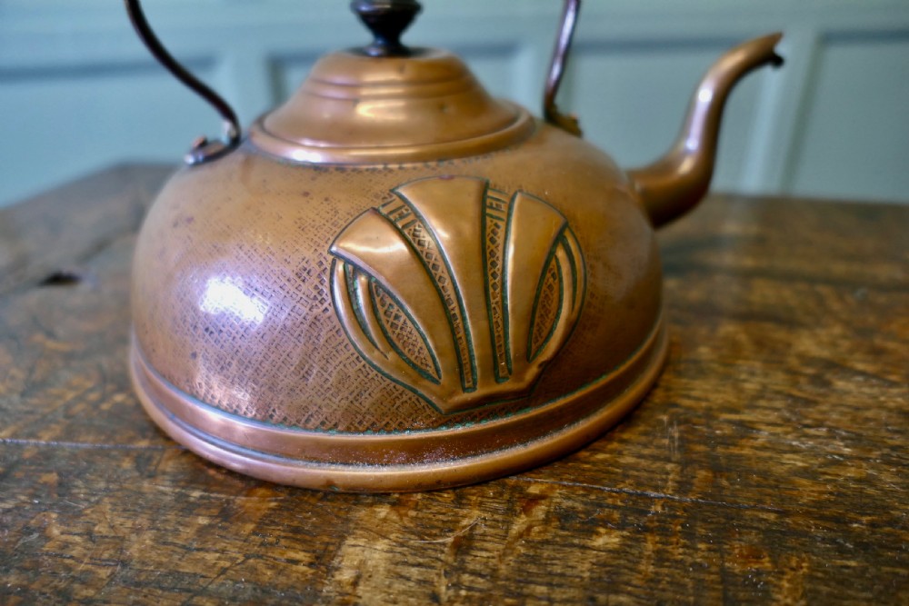 An Arts and Crafts copper kettle with a stylised relief shell motif, gooseneck spout, and turned black wooden handle. View IV