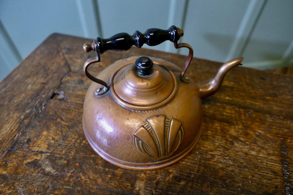An Arts and Crafts copper kettle with a stylised relief shell motif, gooseneck spout, and turned black wooden handle. View V