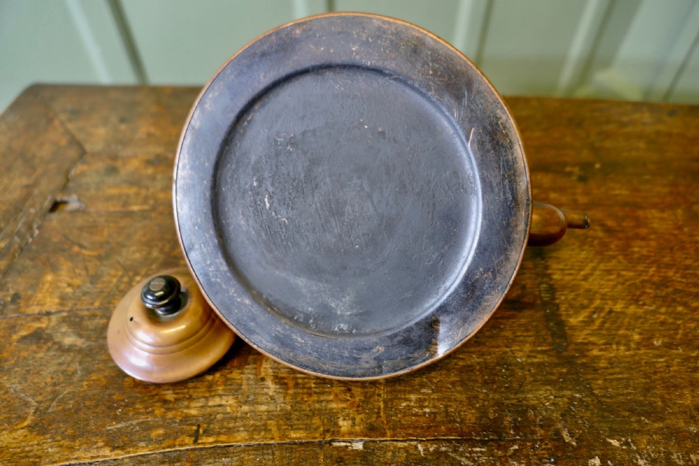 An Arts and Crafts copper kettle with a stylised relief shell motif, gooseneck spout, and turned black wooden handle. View VI