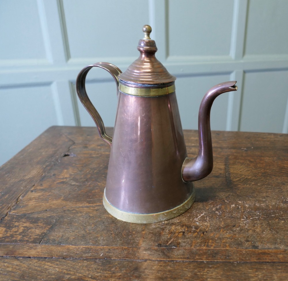 An Arts and Crafts copper coffee or chocolate pot with a conical body, brass collar, arched spout, strap handle, and finial lid. View IV