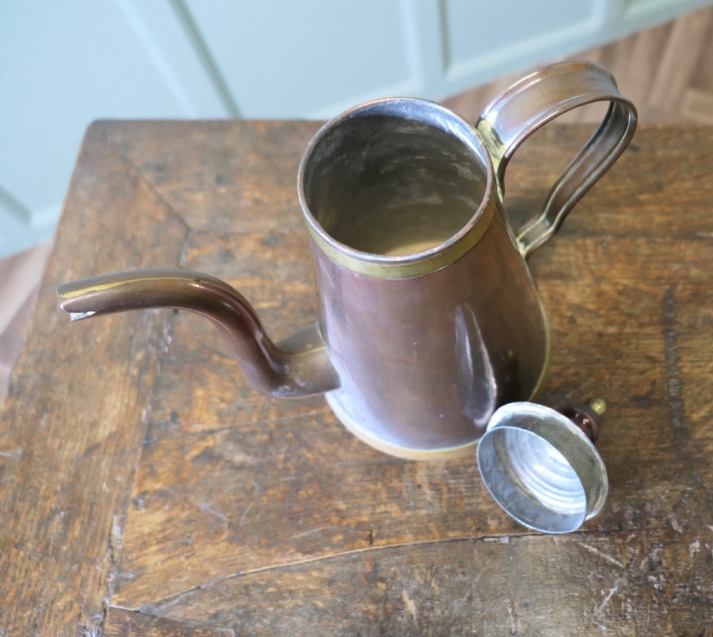 An Arts and Crafts copper coffee or chocolate pot with a conical body, brass collar, arched spout, strap handle, and finial lid. View V