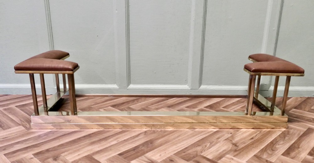 An Art Deco polished brass club fender featuring two corner seats upholstered in tan leather.