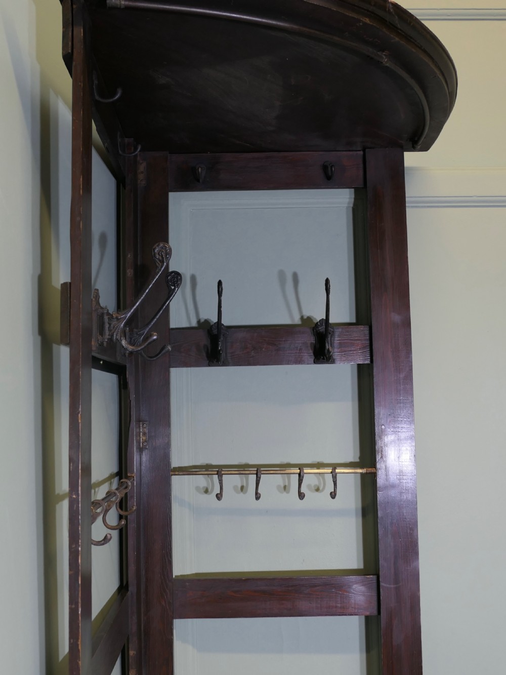 A tall, dark wooden corner coat stand featuring a hinged open framework, top shelf, cast iron coat hooks, and a brass hanging rail. View VII