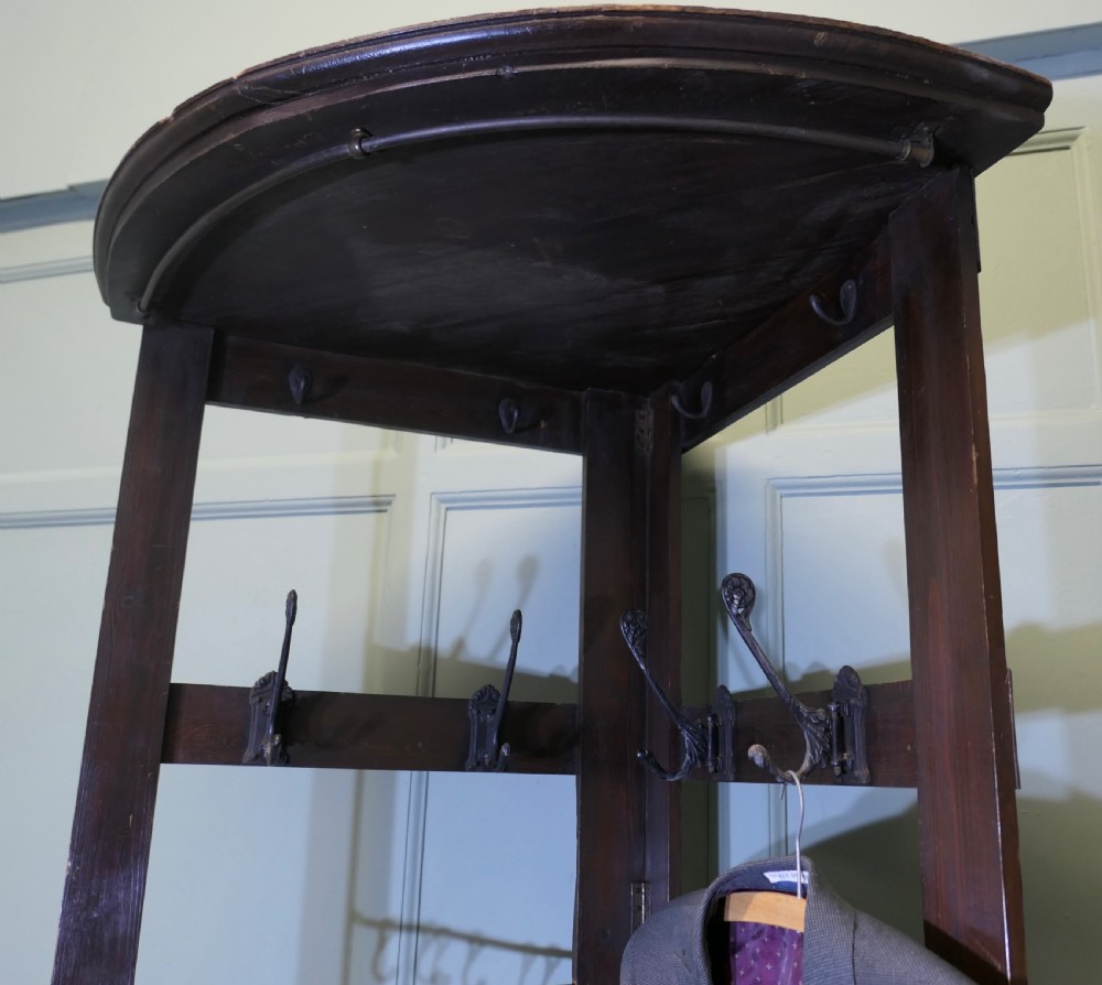 A tall, dark wooden corner coat stand featuring a hinged open framework, top shelf, cast iron coat hooks, and a brass hanging rail. View XII