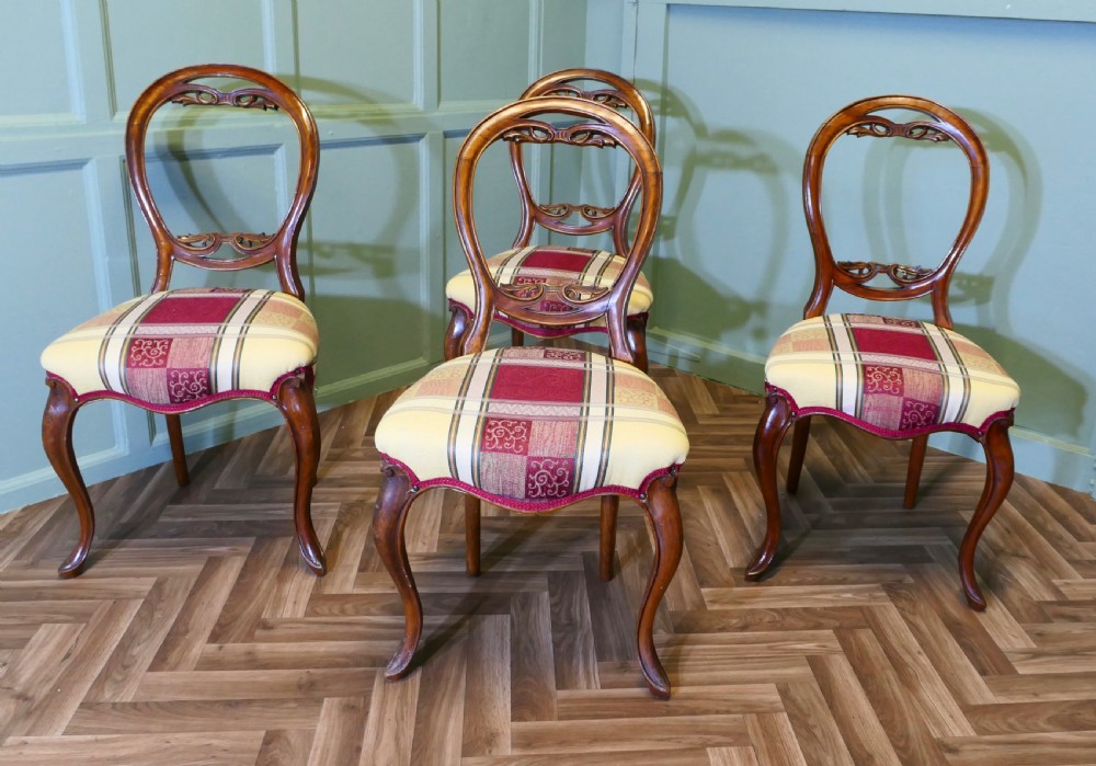 A set of four Victorian mahogany dining chairs featuring carved balloon-shaped backframes, cabriole front legs, and patterned upholstered seats.