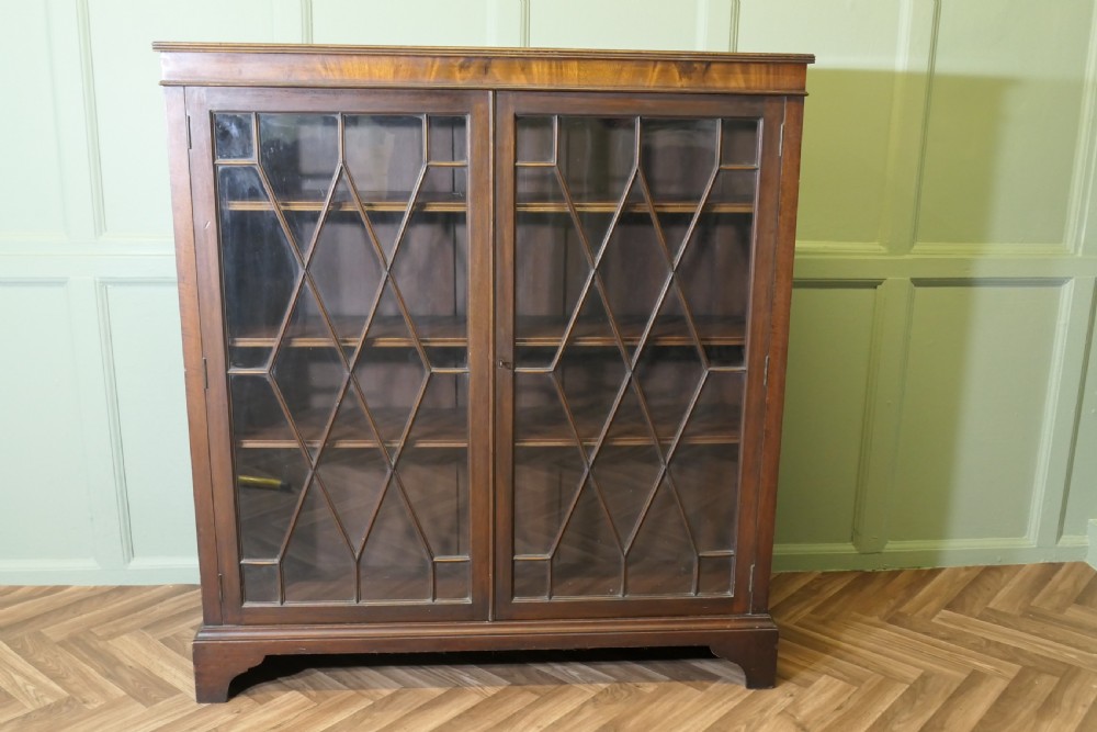 An Edwardian mahogany bookcase featuring two astragal glazed glass doors with geometric lattice patterns, internal wooden shelves, and bracket feet. View II