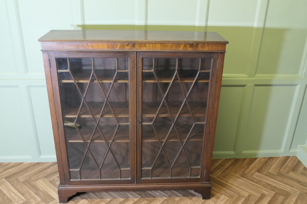 An Edwardian mahogany bookcase featuring two astragal glazed glass doors with geometric lattice patterns, internal wooden shelves, and bracket feet. View III