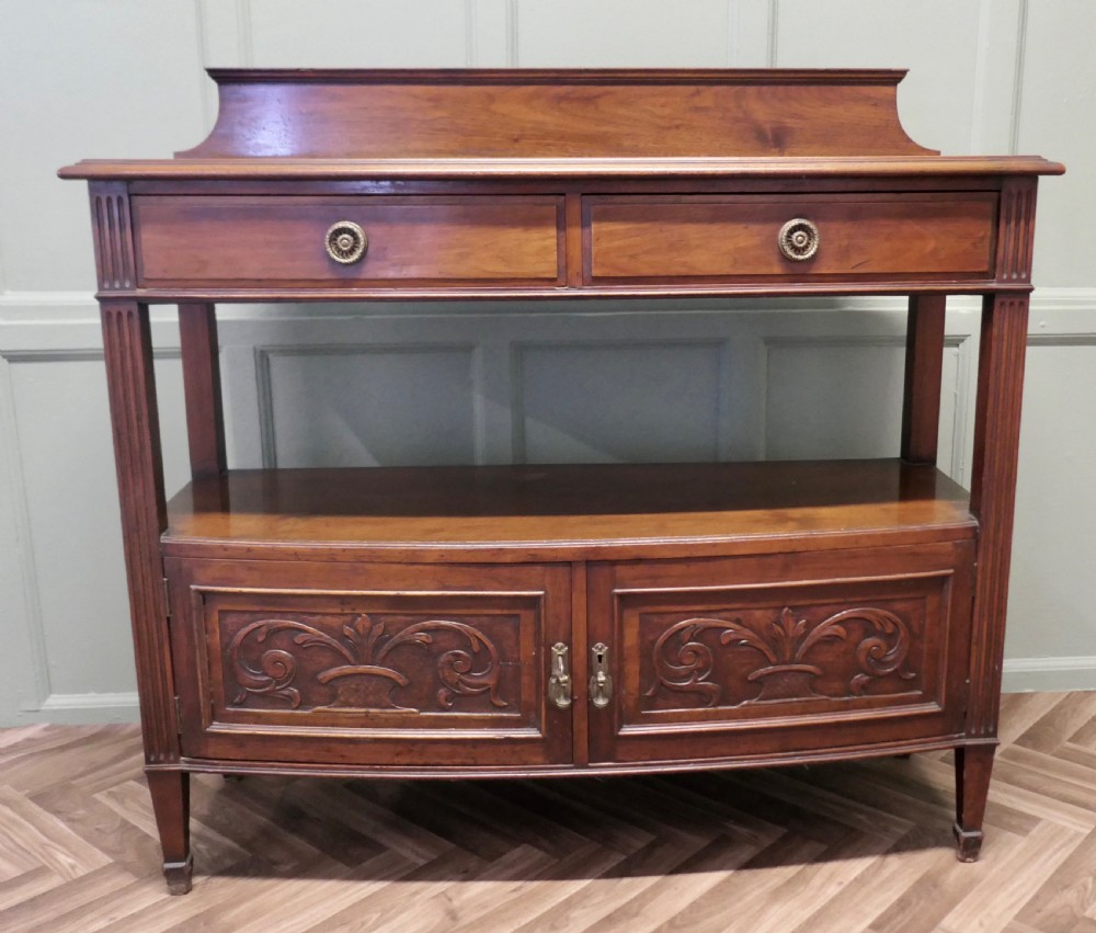 A carved warm brown walnut sideboard featuring two upper drawers, an open lower tier, two carved cupboard doors, fluted side columns, and a raised top gallery.