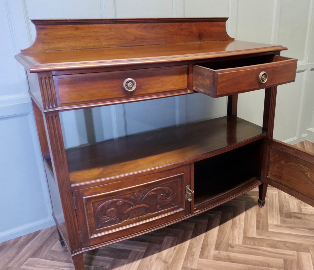 A carved warm brown walnut sideboard featuring two upper drawers, an open lower tier, two carved cupboard doors, fluted side columns, and a raised top gallery. View V
