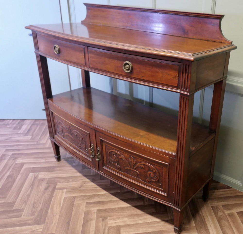 A carved warm brown walnut sideboard featuring two upper drawers, an open lower tier, two carved cupboard doors, fluted side columns, and a raised top gallery. View VI
