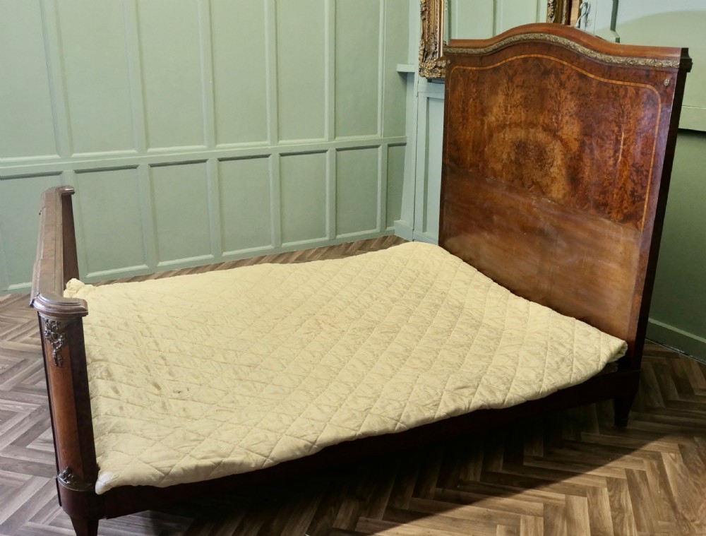 An Art Deco French style double bed featuring a shaped burr walnut headboard and footboard with gilt metal mounts.