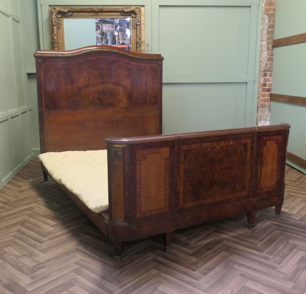 An Art Deco French style double bed featuring a shaped burr walnut headboard and footboard with gilt metal mounts. View VI