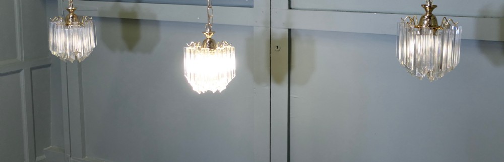 A set of three Art Deco style chandeliers featuring tiered vertical clear crystal prisms hanging from polished brass caps.