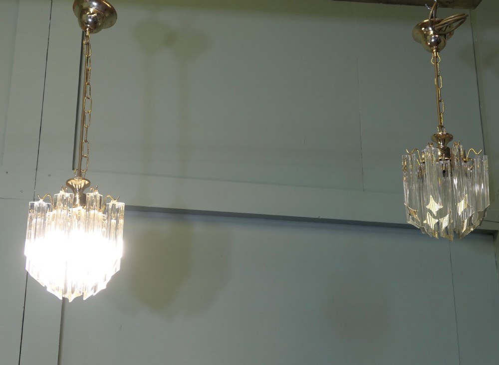 A set of three Art Deco style chandeliers featuring tiered vertical clear crystal prisms hanging from polished brass caps. View IV