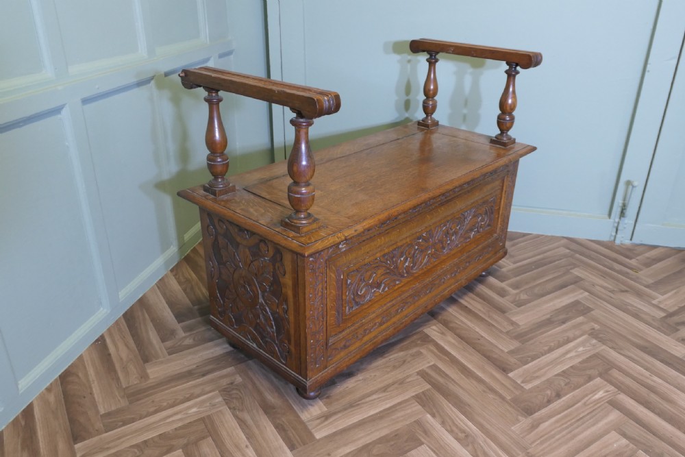 Carved golden oak storage coffer hall seat featuring a central Green Man mask relief carving and raised turned baluster arm supports. View III