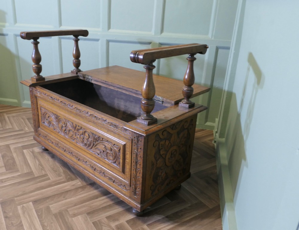Carved golden oak storage coffer hall seat featuring a central Green Man mask relief carving and raised turned baluster arm supports. View V