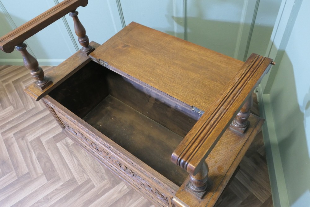 Carved golden oak storage coffer hall seat featuring a central Green Man mask relief carving and raised turned baluster arm supports. View VI