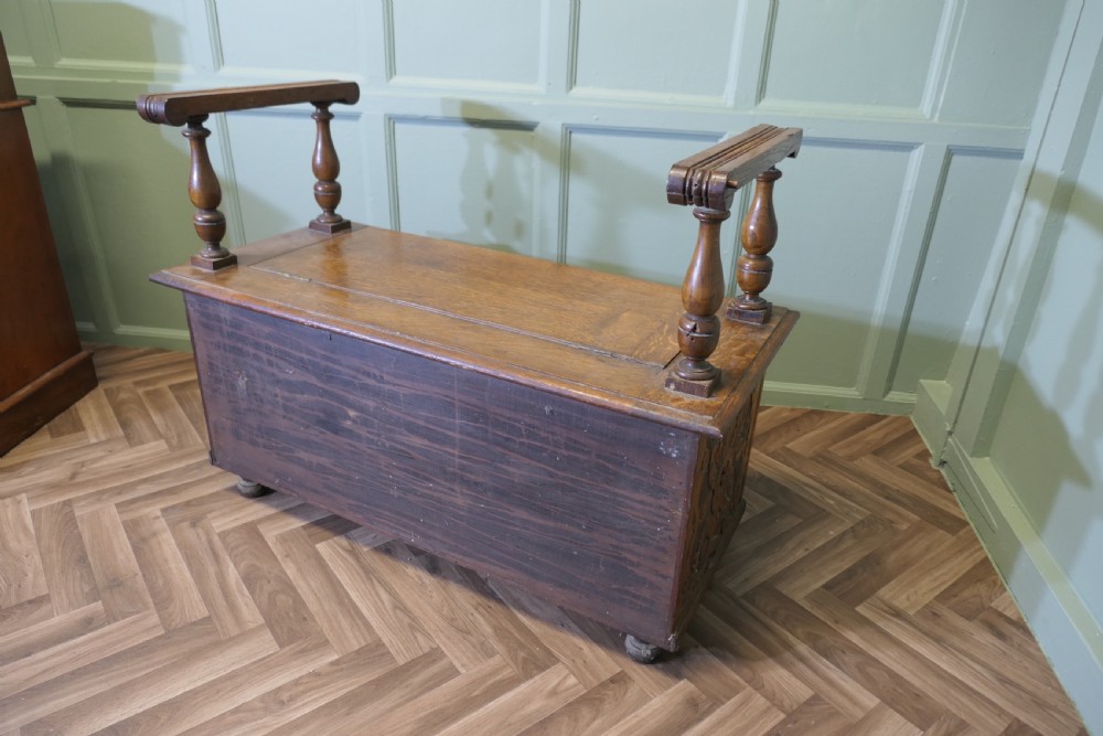 Carved golden oak storage coffer hall seat featuring a central Green Man mask relief carving and raised turned baluster arm supports. View VII