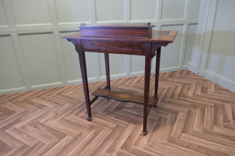 An Edwardian satin walnut ladies writing desk featuring a top superstructure with brass gallery, single drawer with marquetry oval inlay, tapered square legs, and an undertier shelf on brass castors. View VII