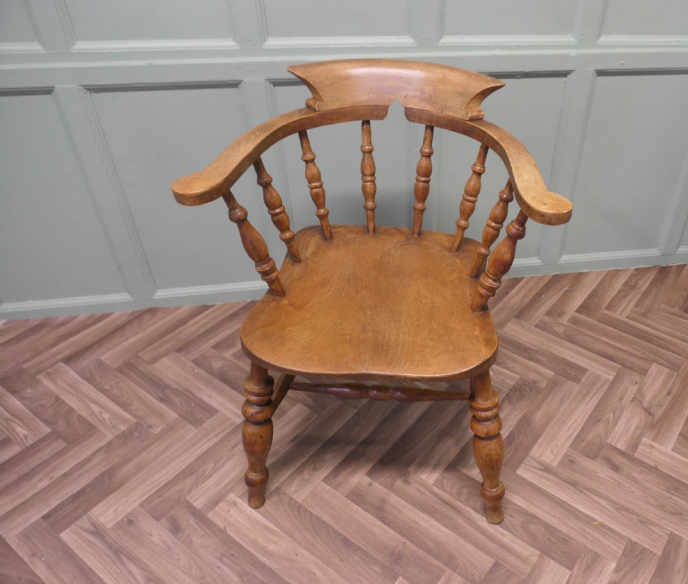 A 19th-century wooden smokers bow armchair featuring a curved crest rail, turned baluster spindles, a carved saddle seat, and turned legs. View II