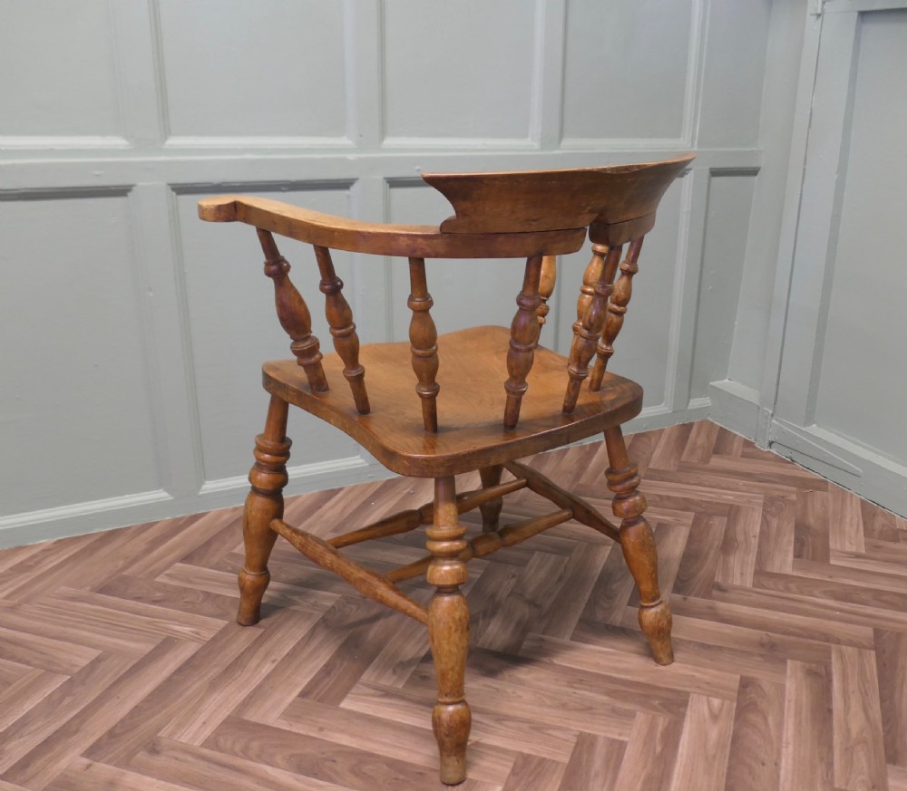 A 19th-century wooden smokers bow armchair featuring a curved crest rail, turned baluster spindles, a carved saddle seat, and turned legs. View V