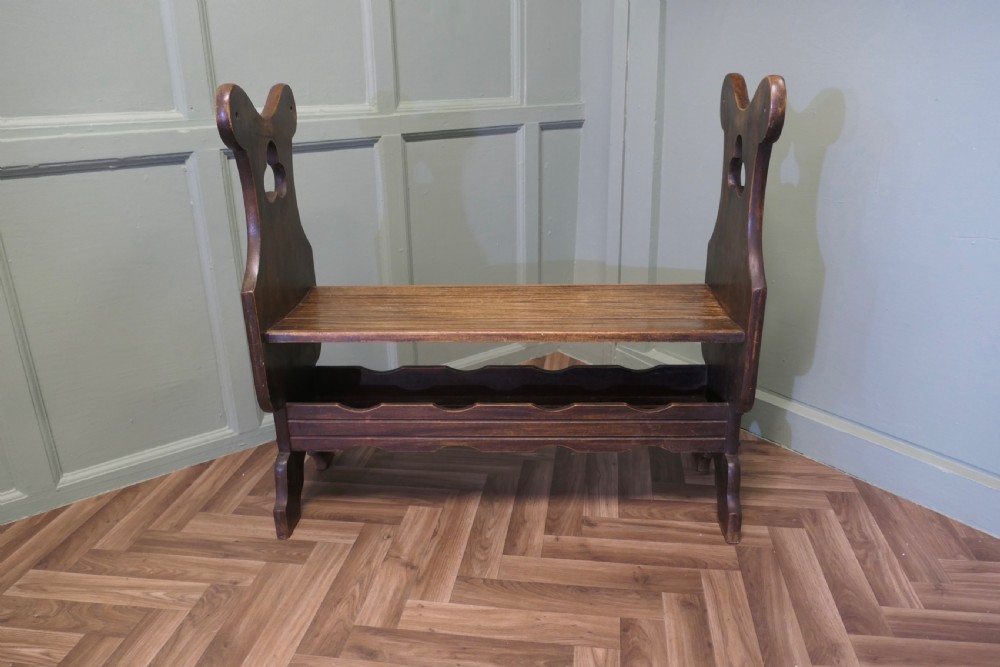 A dark walnut hall bench with high cutout side supports, a flat wooden seat, and a lower scalloped shelf for shoe storage.
