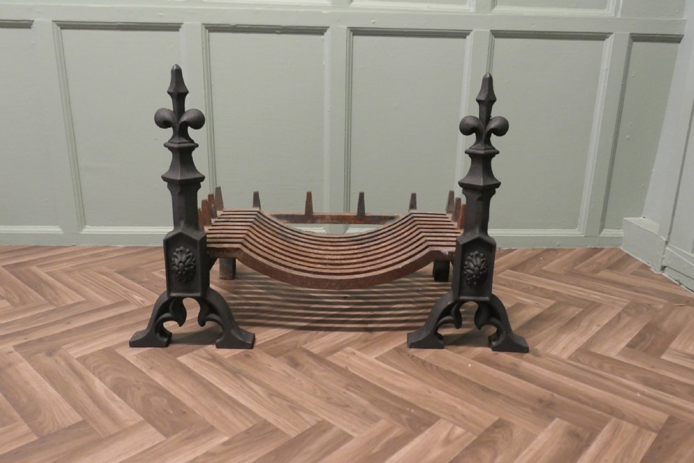 A nineteenth-century dark cast iron fire grate featuring twin fire dogs topped with fleur-de-lis finials and a curved slatted central log cradle.