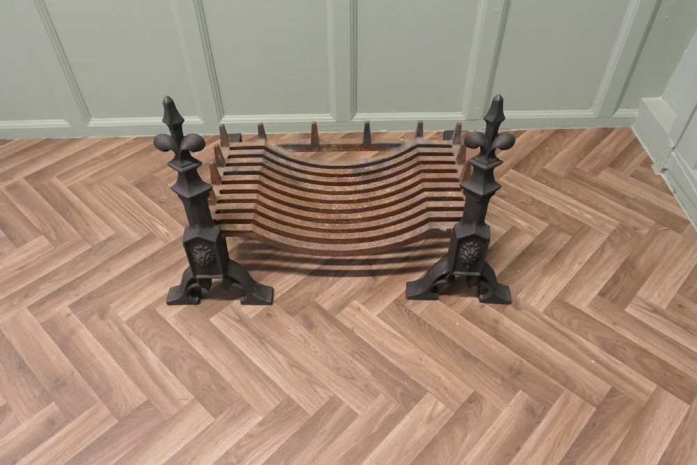 A nineteenth-century dark cast iron fire grate featuring twin fire dogs topped with fleur-de-lis finials and a curved slatted central log cradle. View II