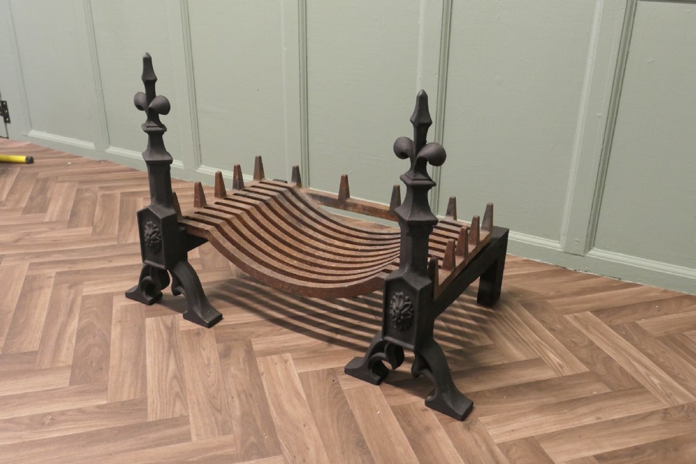 A nineteenth-century dark cast iron fire grate featuring twin fire dogs topped with fleur-de-lis finials and a curved slatted central log cradle. View III