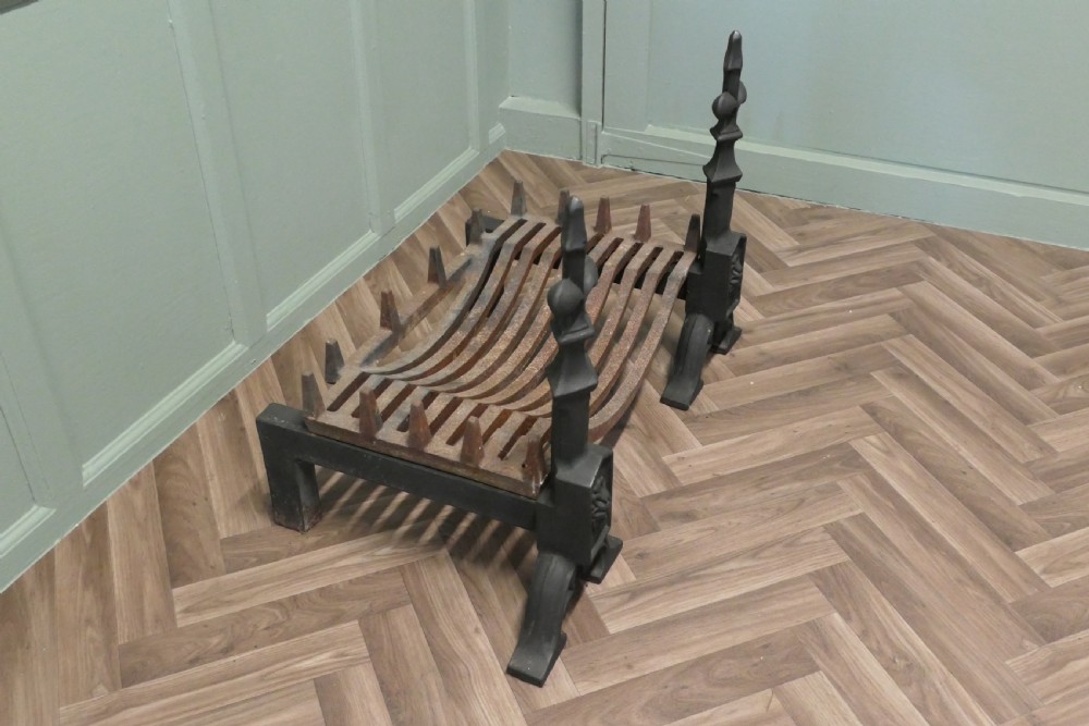 A nineteenth-century dark cast iron fire grate featuring twin fire dogs topped with fleur-de-lis finials and a curved slatted central log cradle. View IV