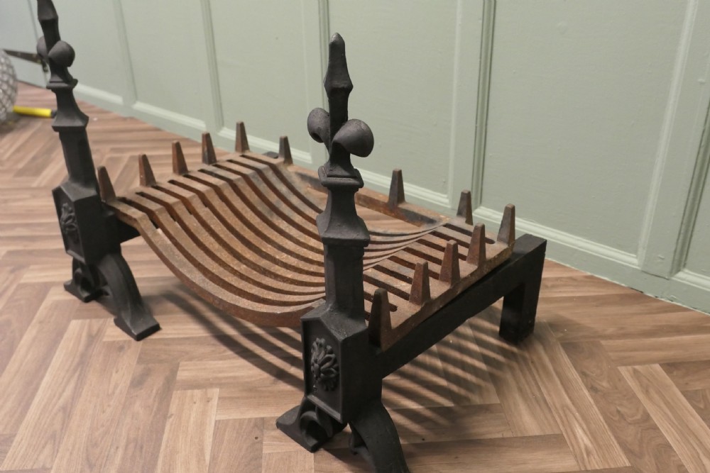 A nineteenth-century dark cast iron fire grate featuring twin fire dogs topped with fleur-de-lis finials and a curved slatted central log cradle. View V