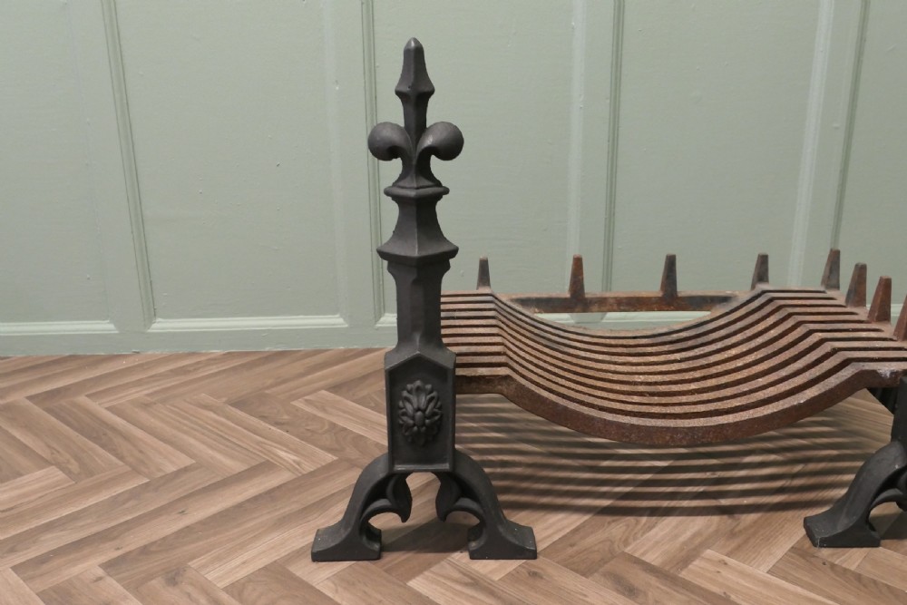 A nineteenth-century dark cast iron fire grate featuring twin fire dogs topped with fleur-de-lis finials and a curved slatted central log cradle. View VI