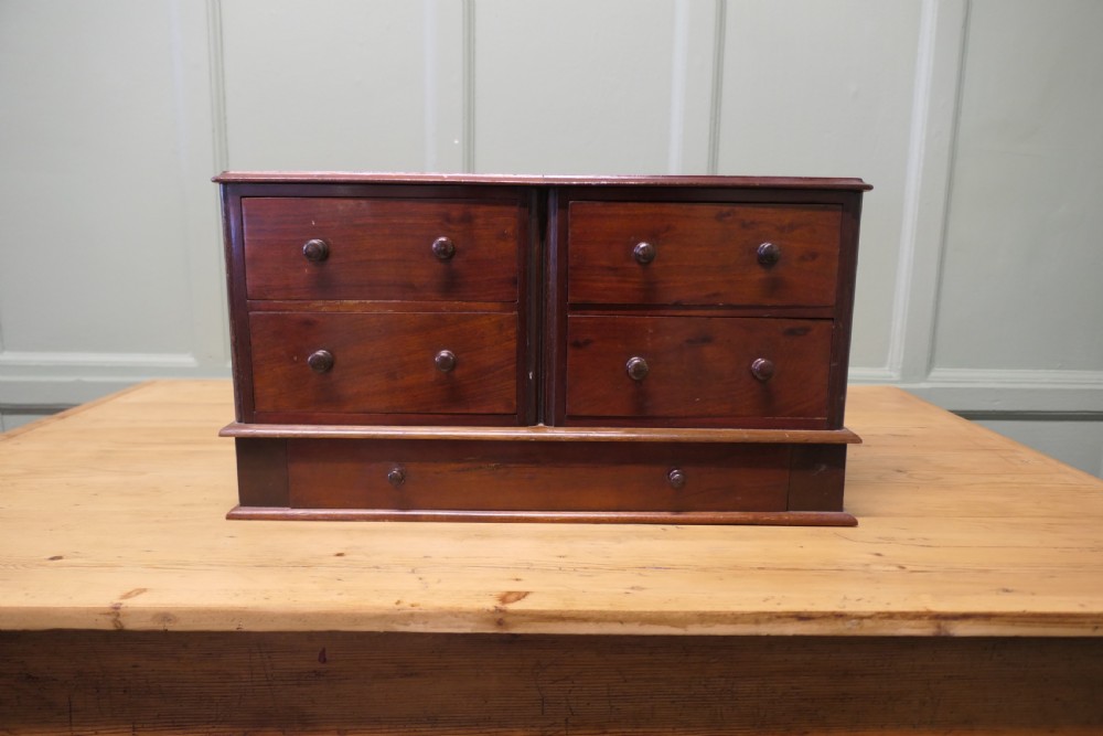 A mahogany desktop cabinet featuring five drawers with turned wooden handles arranged in two upper rows and one lower wide drawer.
