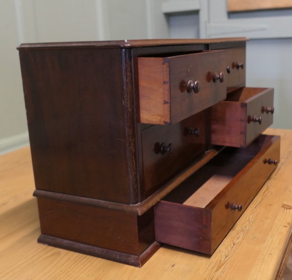 A mahogany desktop cabinet featuring five drawers with turned wooden handles arranged in two upper rows and one lower wide drawer. View V