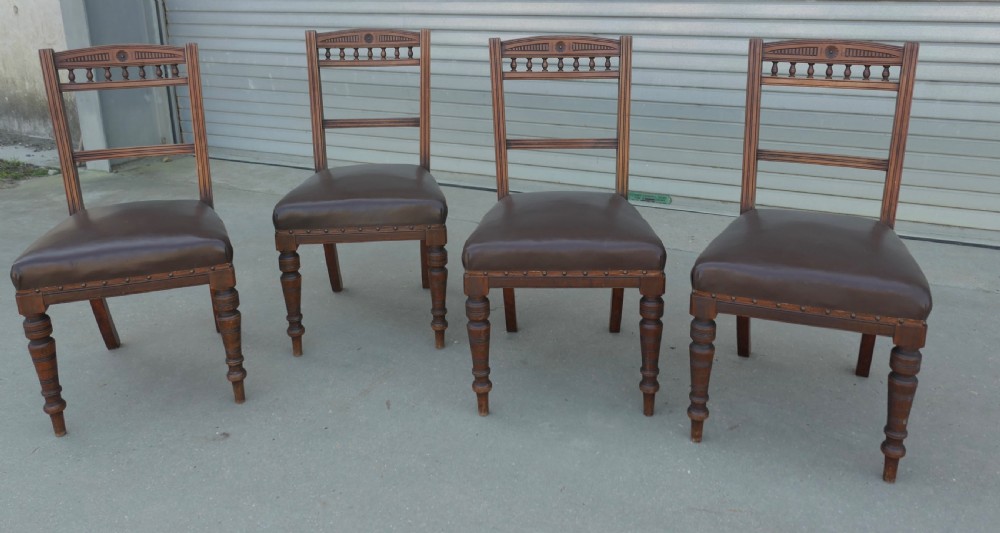 A set of four Edwardian carved oak dining chairs featuring brown leather upholstered seats, turned front legs, and carved crest rails.