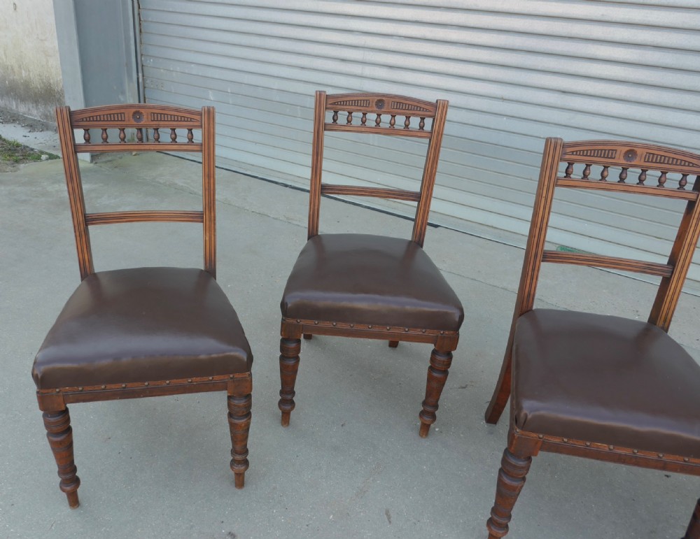 A set of four Edwardian carved oak dining chairs featuring brown leather upholstered seats, turned front legs, and carved crest rails. View II