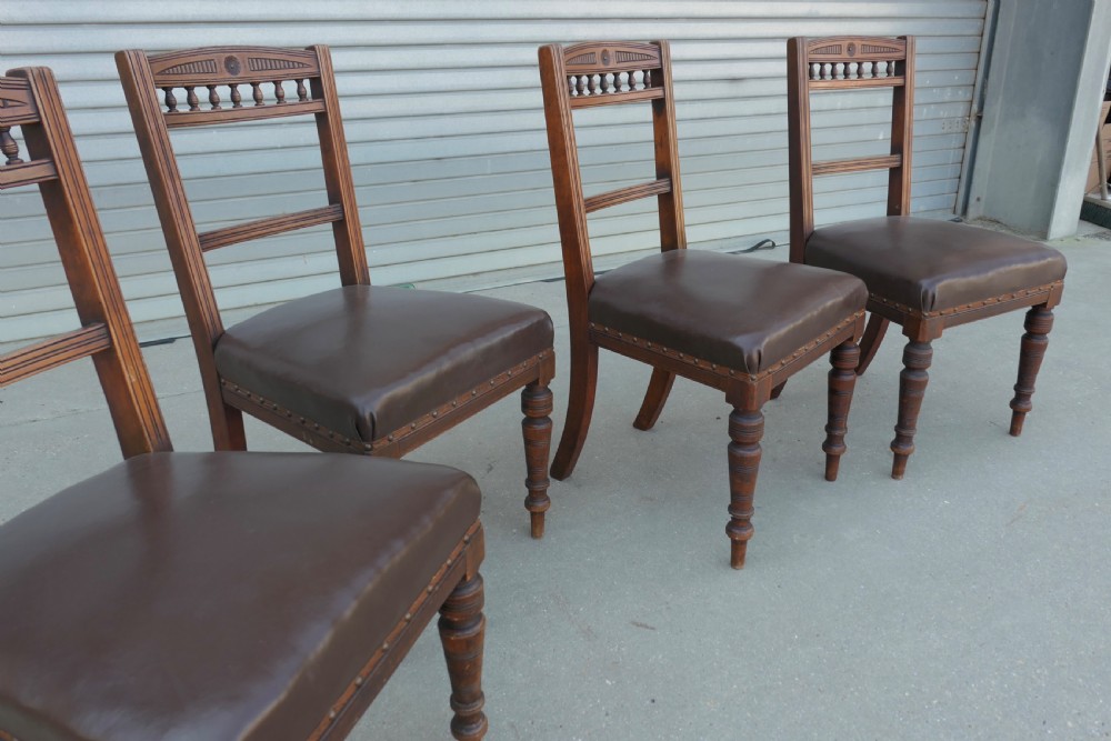 A set of four Edwardian carved oak dining chairs featuring brown leather upholstered seats, turned front legs, and carved crest rails. View III