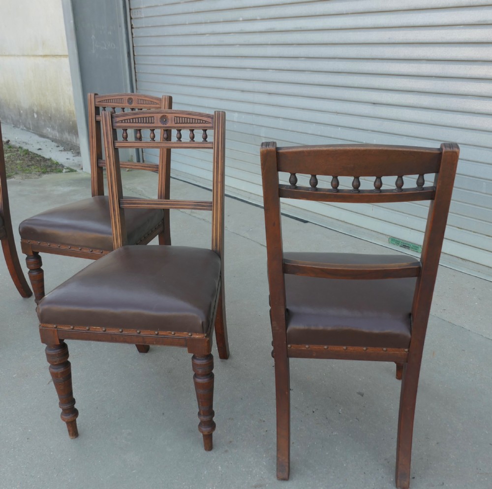 A set of four Edwardian carved oak dining chairs featuring brown leather upholstered seats, turned front legs, and carved crest rails. View IV