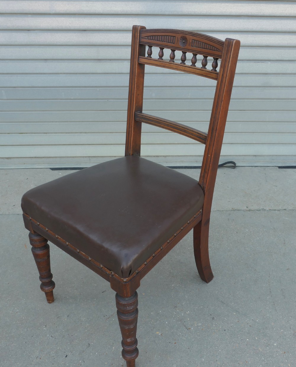 A set of four Edwardian carved oak dining chairs featuring brown leather upholstered seats, turned front legs, and carved crest rails. View V