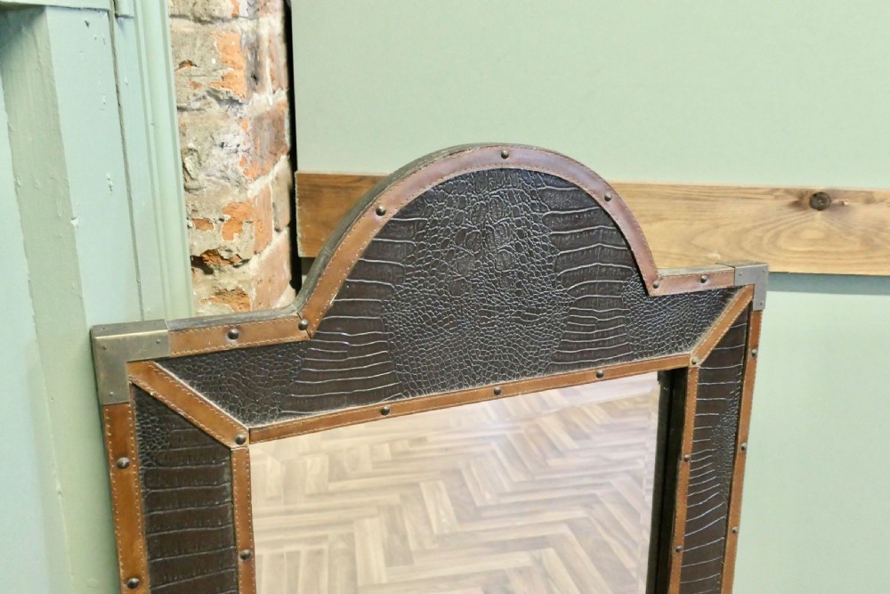 An Art Deco wall mirror featuring a dark crocodile-embossed leather frame with tan leather borders, brass stud details, and an arched crest. View V
