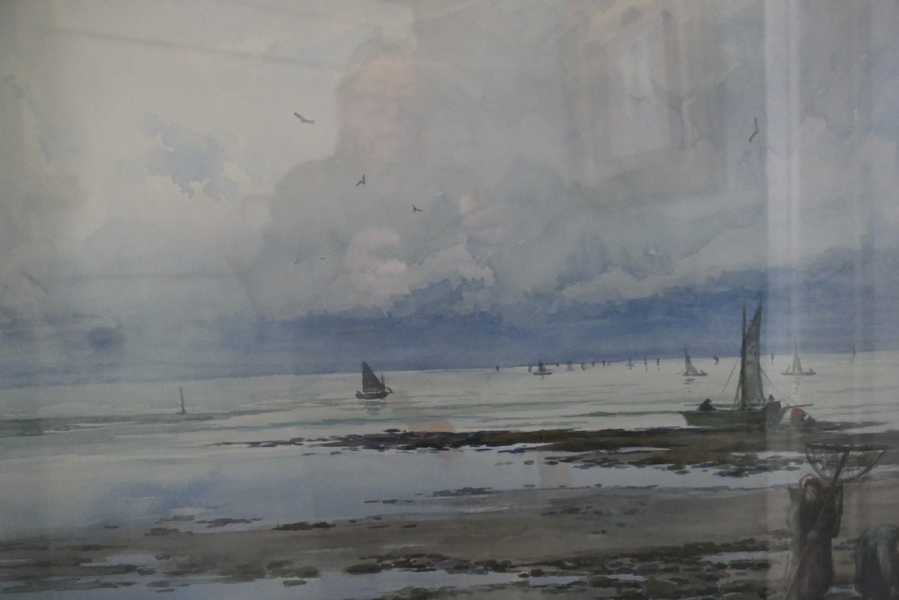 A framed coastal watercolour painting featuring figures on a shore with fishing boats in the distance beneath a cloudy blue sky. View III