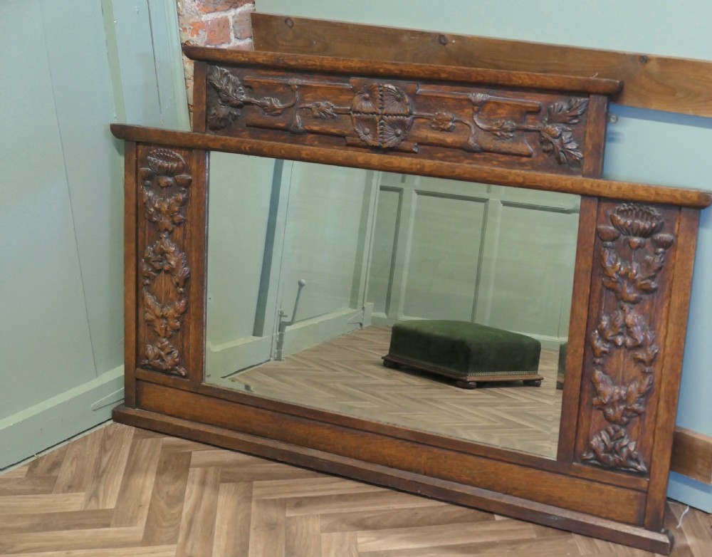 A large Arts and Crafts oak overmantel mirror featuring detailed relief carvings of thistles and stylized leaves around a rectangular glass mirror. View II